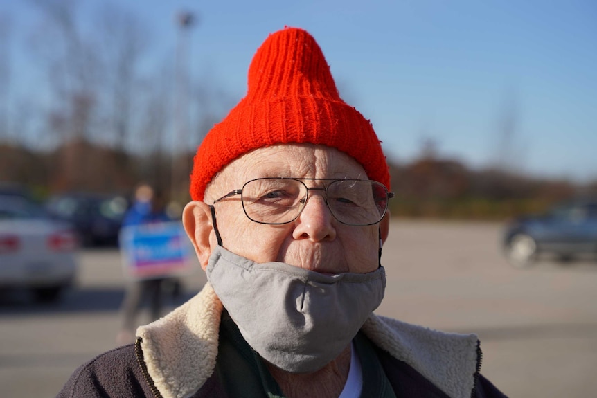A man in a red beanie wears a grey mask on his chin instead of his nose