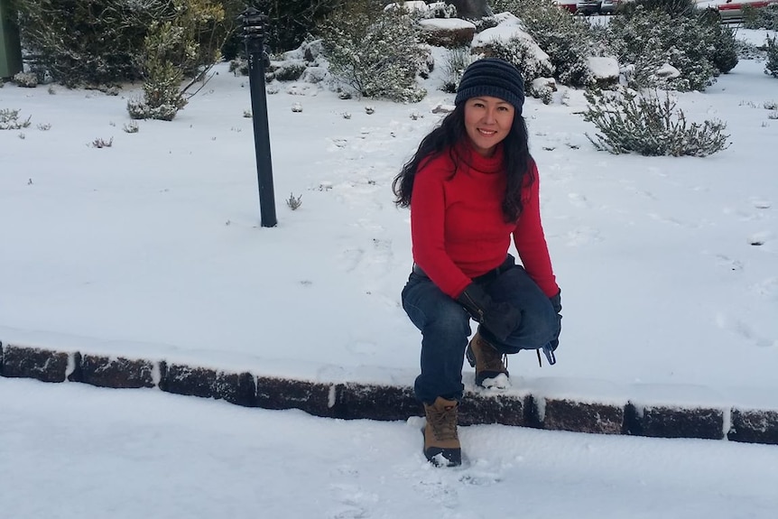 A woman in red crouches on a snow field.