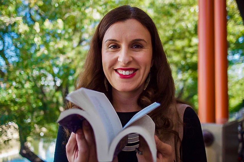 A woman holding a book and smiling to camera