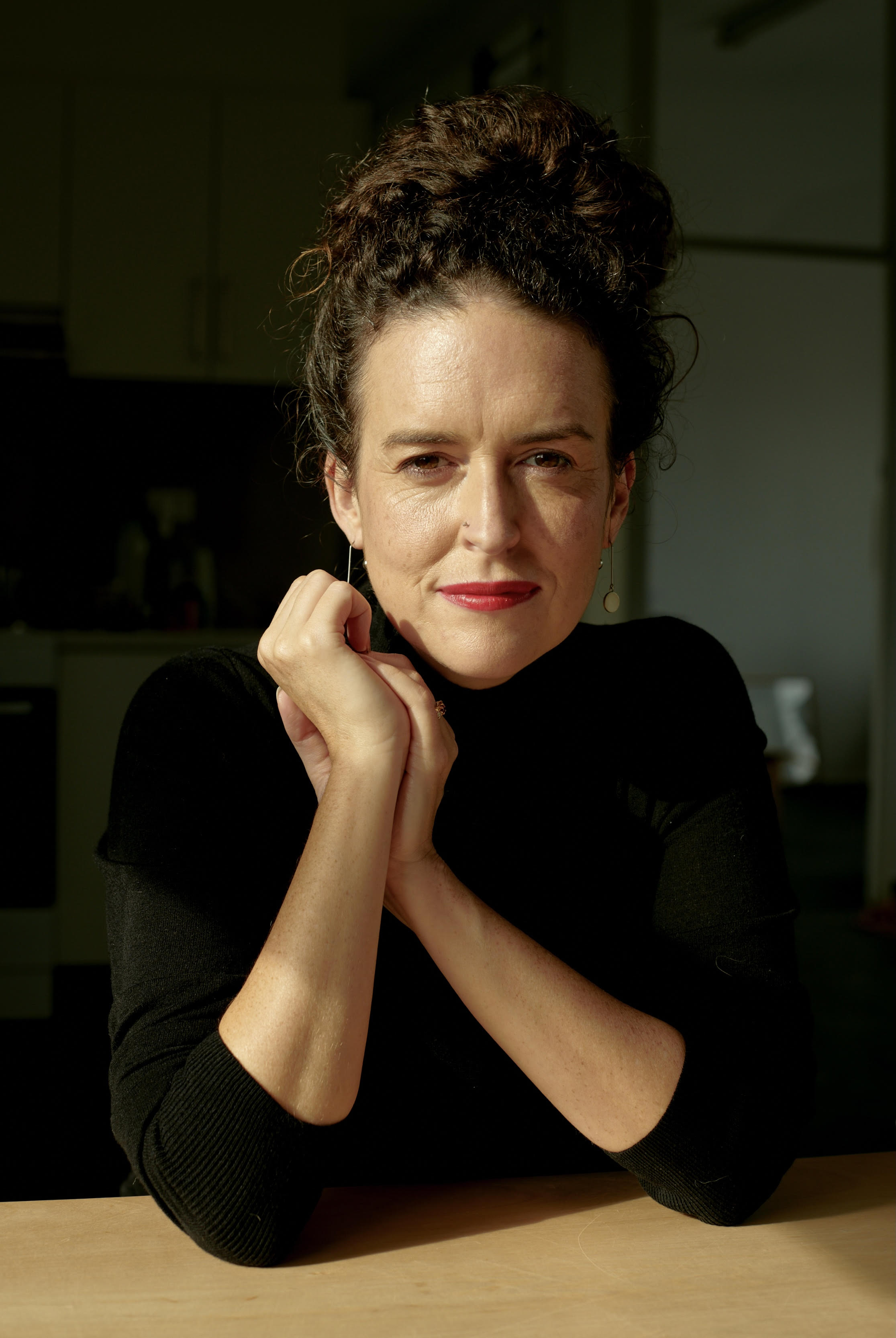 A 40-something brunette woman with her curly hair pulled back on top of her head. She sits with her elbows on a table. 