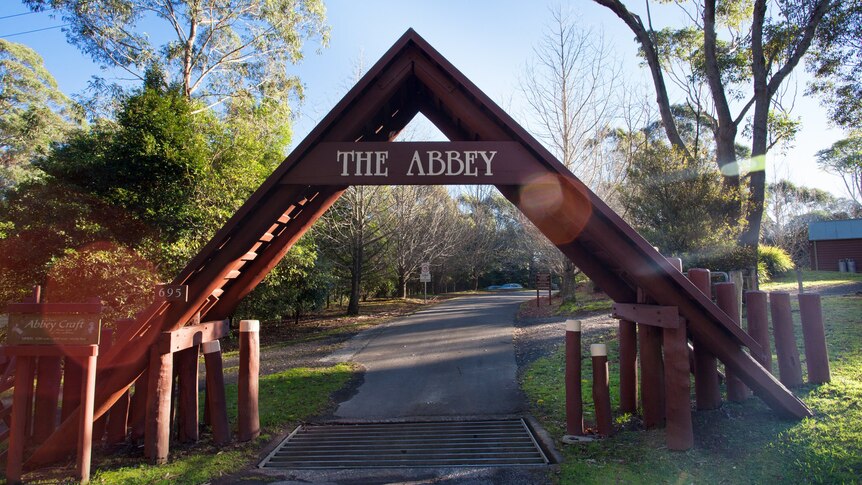 A large wooden outdoor A-framed structure, with 'The Abbey' written at the top. Bush surrounds it.