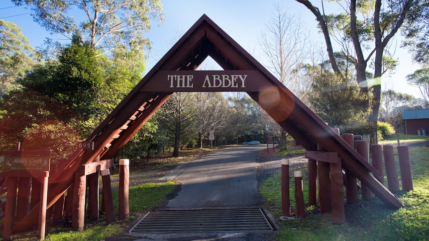 A large wooden outdoor A-framed structure, with 'The Abbey' written at the top. Bush surrounds it.