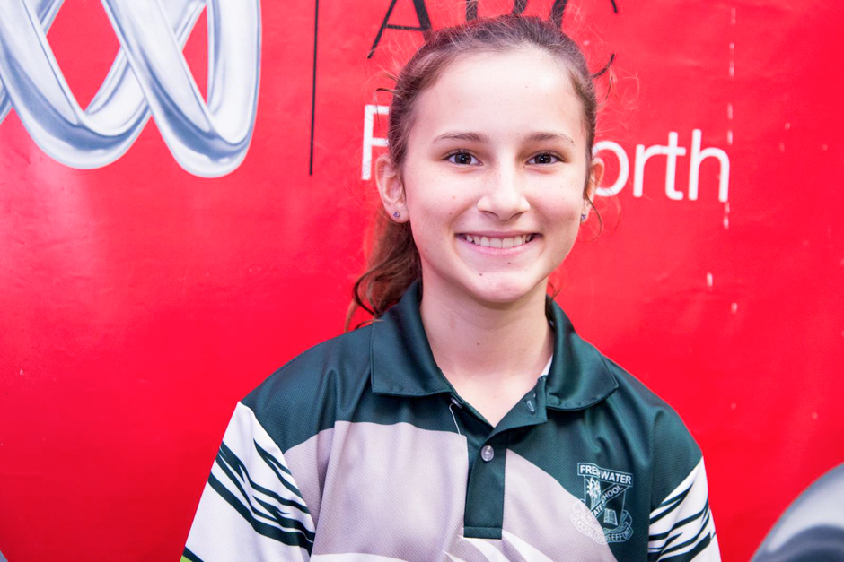 A year six girl stands in front of a bright red banner.