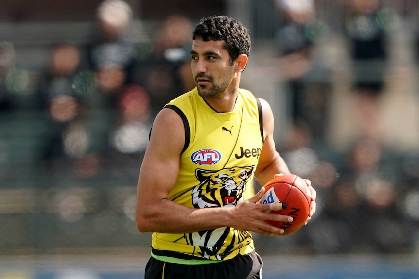 A Richmond Tigers AFL player wears a yellow guernsey holding a ball