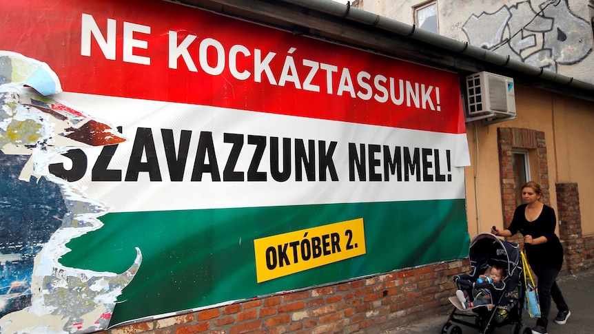 A woman pushes a stroller with her child in front of the Hungarian government's poster regarding the referendum.