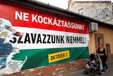 A woman pushes a stroller with her child in front of the Hungarian government's poster regarding the referendum.