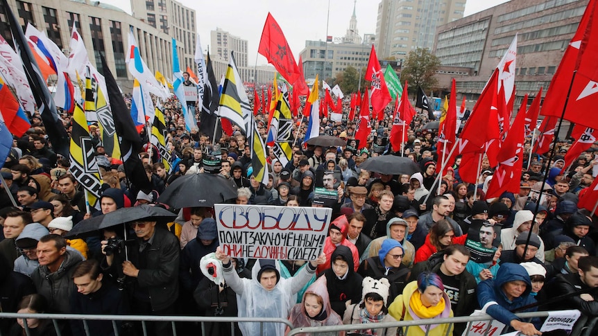 Thousands of protesters stand together, with many holding signs and flags