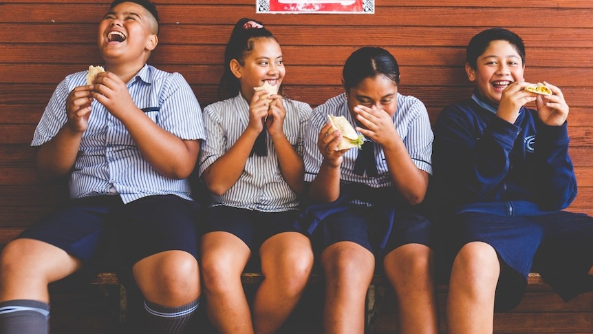 Young Pacific children sitting on a bench eating and laughing