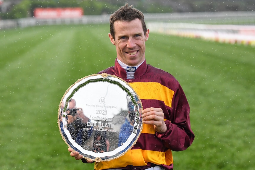 A jockey smiles as he holds the Cox Plate after winning the 2021 race.