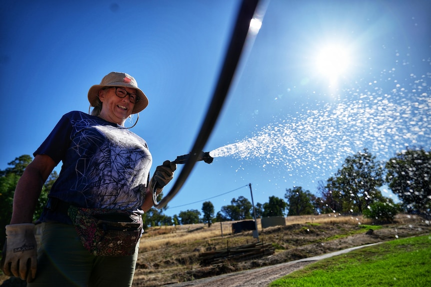A woman smiles as she shoots water from a hose.