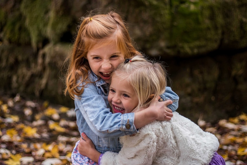 Two young girls hugging each other and smiling to demonstrate how to teach kids to be good losers and winners.