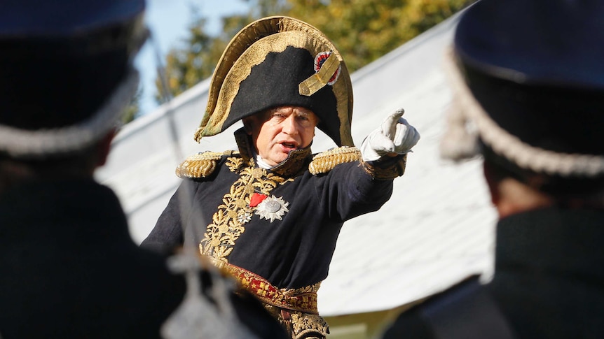 A man dressed as Napoleon rides a horse.