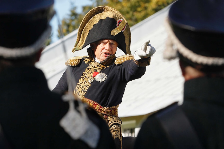 A man dressed as Napoleon rides a horse.