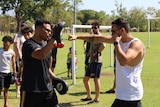 Two men in sunglasses are pictured, one holds boxing pads while the other's arm is stretched out to hit the pad.