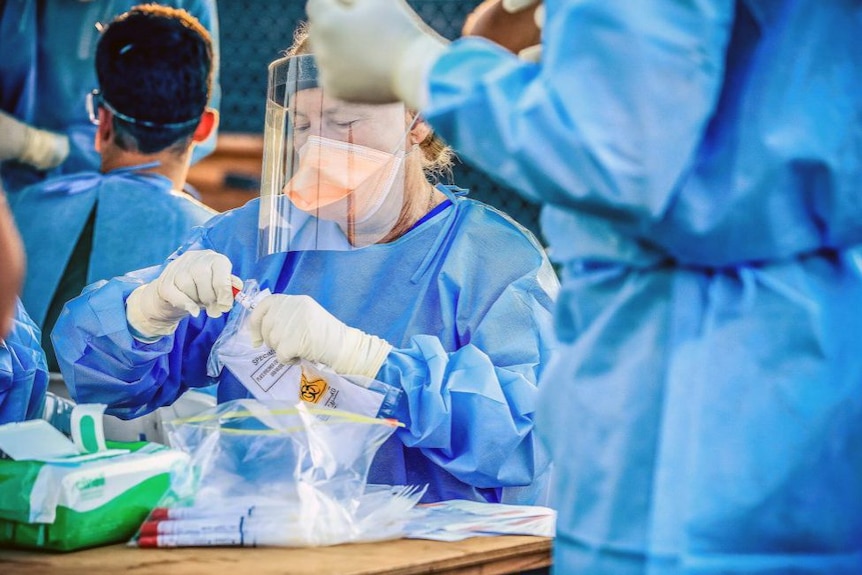 Nurse standing in blue coat holding test tube and wearing mask. 