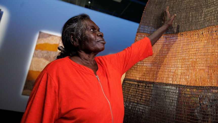 Artist Margaret Rarru Garrawurra stands in front of her prize winning, woven artwork.