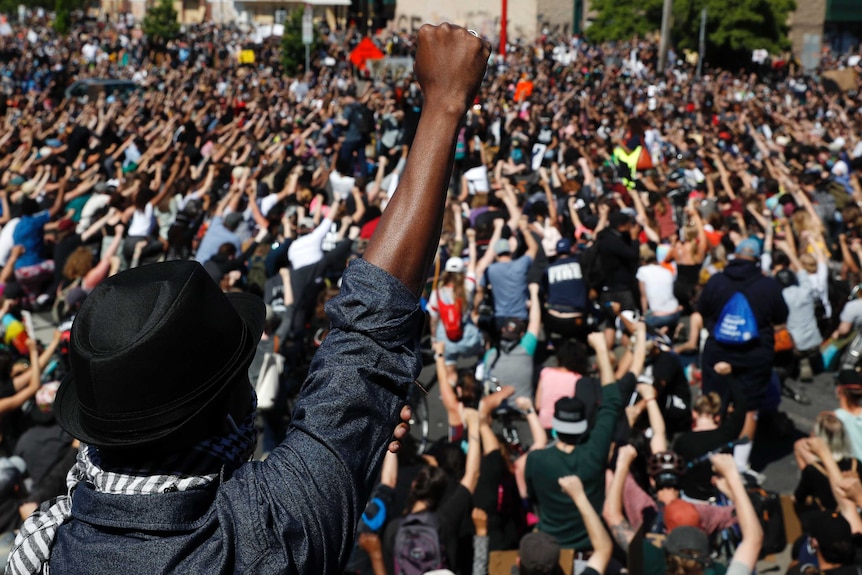 Thousands of people are shown with their fists in the air as they face the opposite direction to the camera.