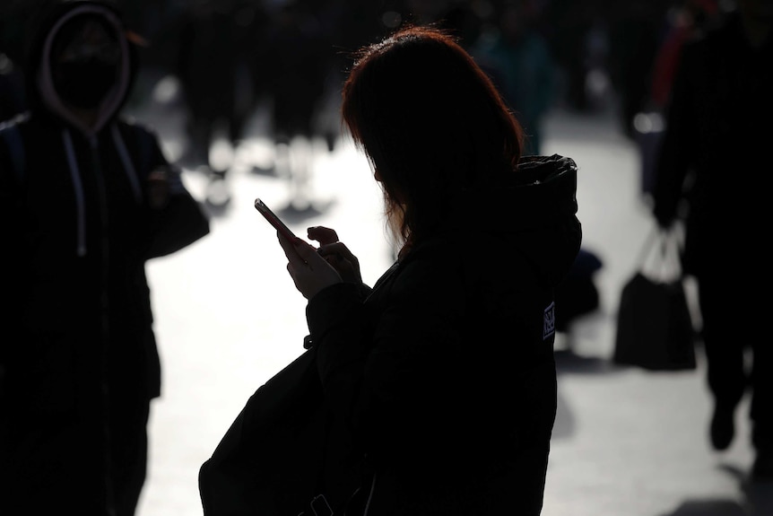 A Chinese woman in silhouette looking at her phone