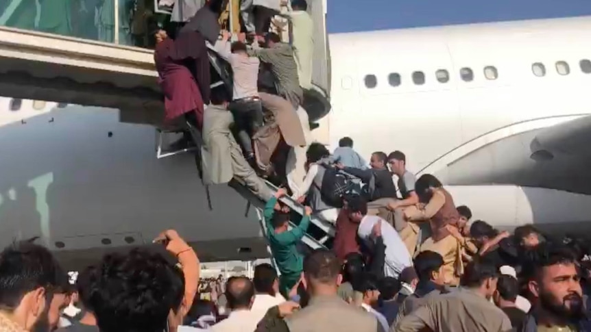 A group of people scramble to climb up stairs with a plane behind them.