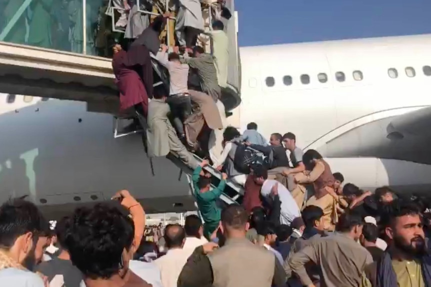 A group of people scramble to climb up stairs with a plane behind them.