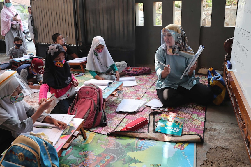 Indonesian students listen to their teacher, who wears a face shield to protect from COVID-19.