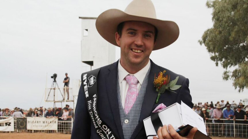 A man wearing a suit and an Akubra at a country race day.