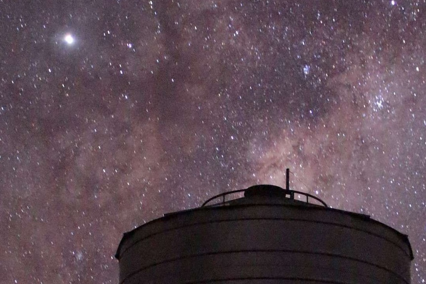 A night sky with one large, bright star with many smaller stars and a silo at the bottom of the image.