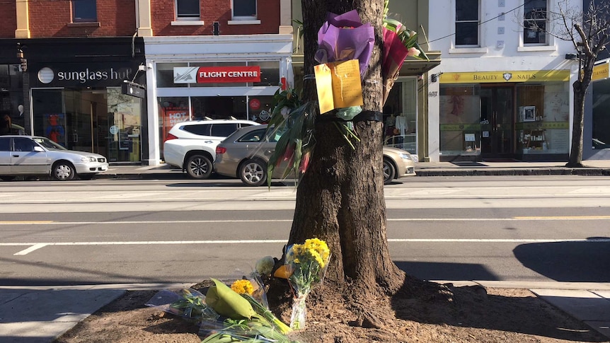 Flowers are laid at the foot of a tree and tied to its trunk to remember a female cyclist who was killed in a hit-and-run.