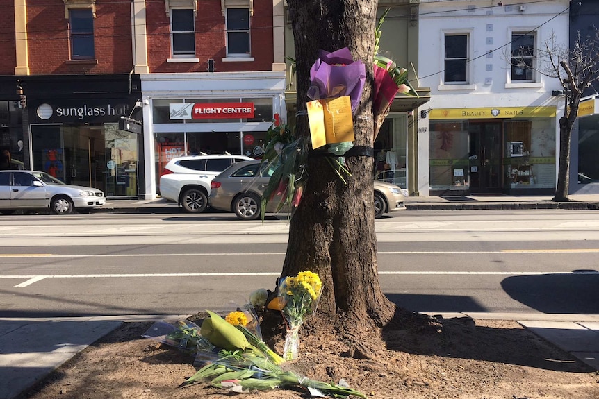 Flowers are laid at the foot of a tree and tied to its trunk to remember a female cyclist who was killed in a hit-and-run.