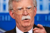 John Bolton speaking into a microphone pointing his finger