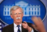 John Bolton speaking into a microphone pointing his finger