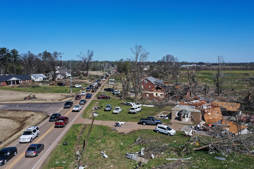 A view of cars backed up on a road and houses that have been destroyed and fallen trees.