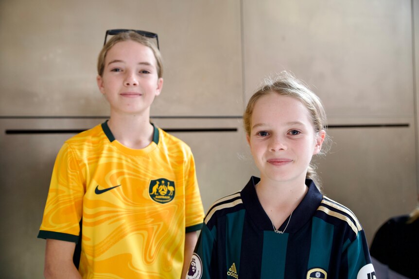 Two young girls with blonde hair wear football shirts