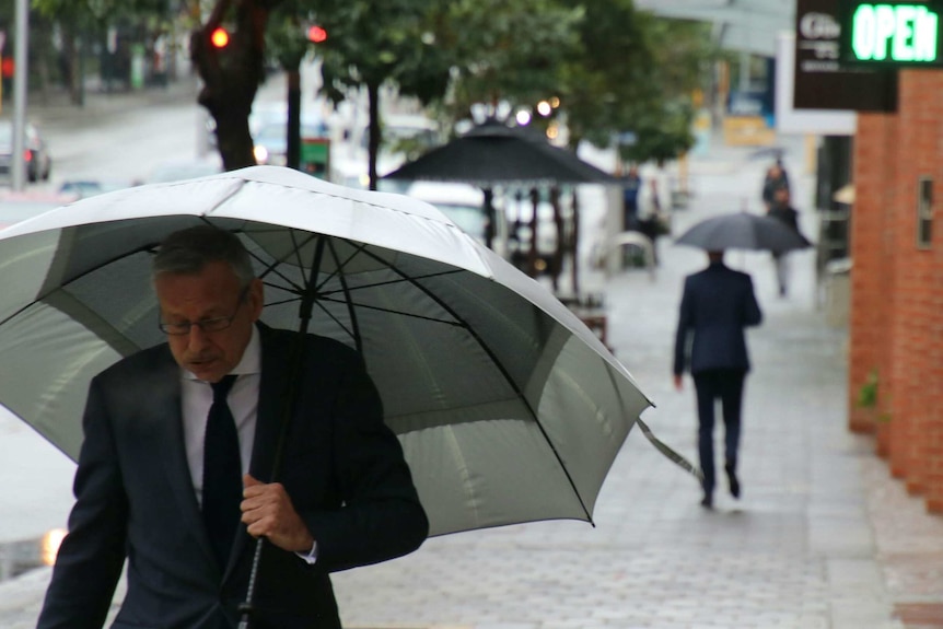 A man holding an umbrella walks along a Perth street.