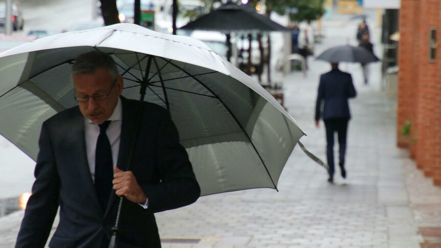 A man holding an umbrella walks along a Perth street.