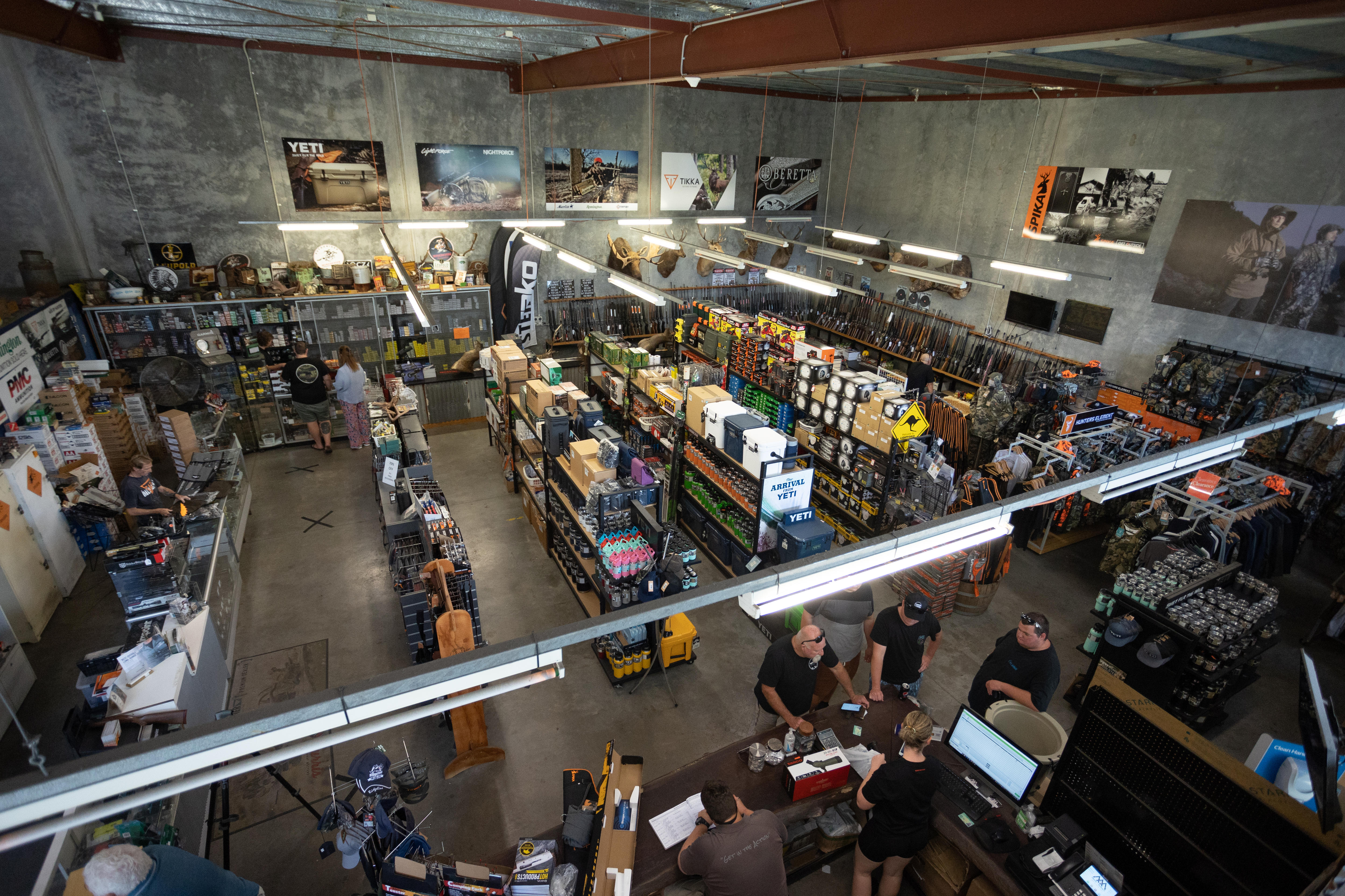 A large warehouse with a high ceiling and shelves of ammunition and supplies, with a rack of guns on the far right.