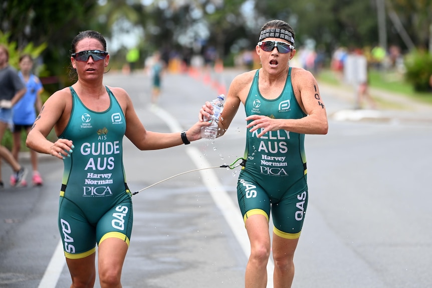 Briarna Silk hands Katie Kelly a bottle of water during the run leg of a para-triathlon.