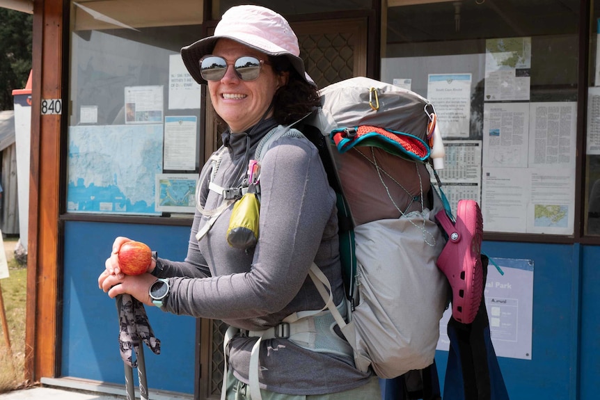 Picture of a woman in bushwalking gear, wearing a pack and holding an apple