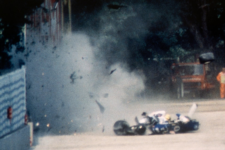 A wreck of an F1 car, recently hitting a wall, with dust, smoke and debris flying in the air