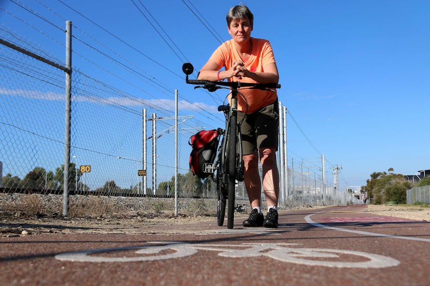 Maxine leans on her bike in a cycle path, with a painted bike symbol in the foreground.