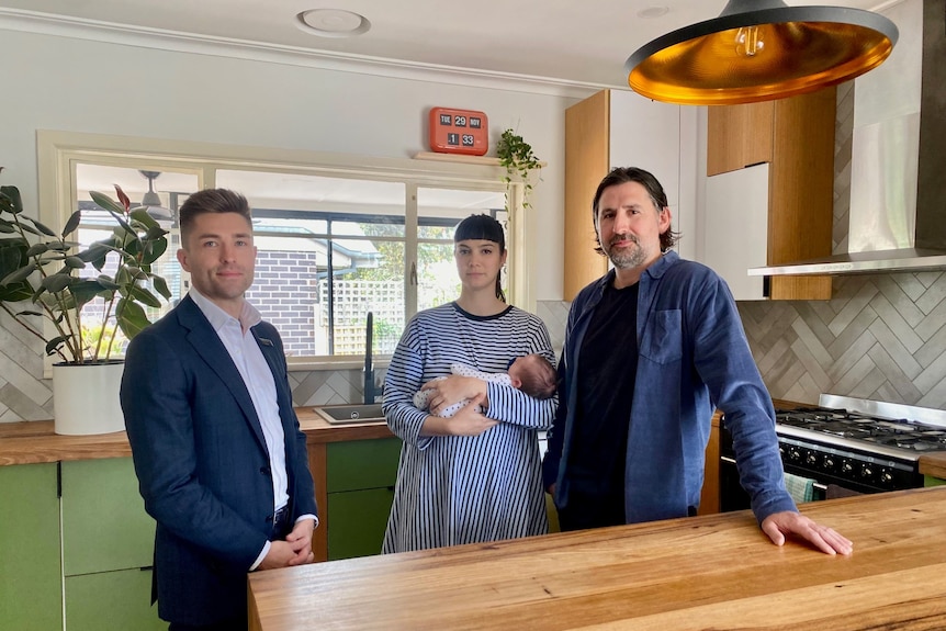 A young male real estate agent stands in the kitchen of his clients who are are a young family