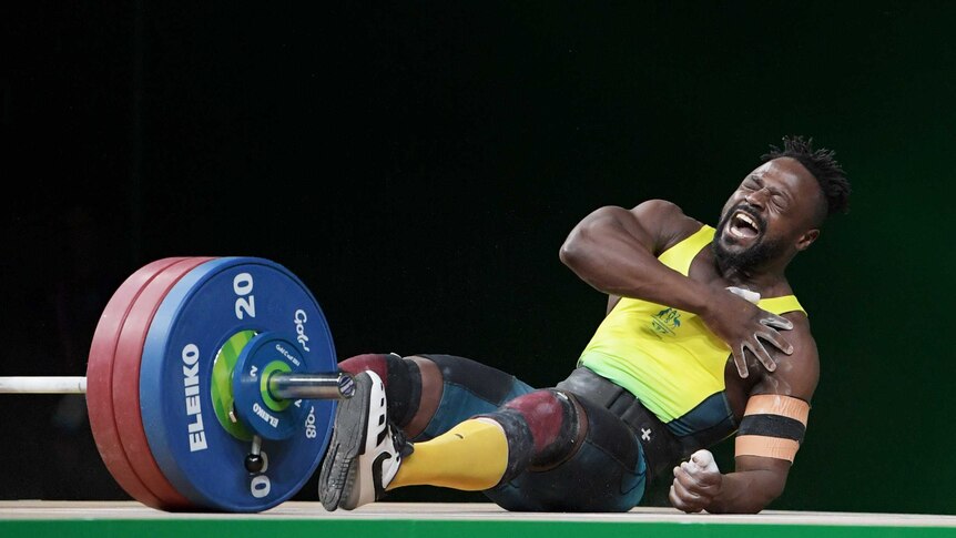 Weightlifter Francois Etoundi clutches his shoulder and falls to the ground