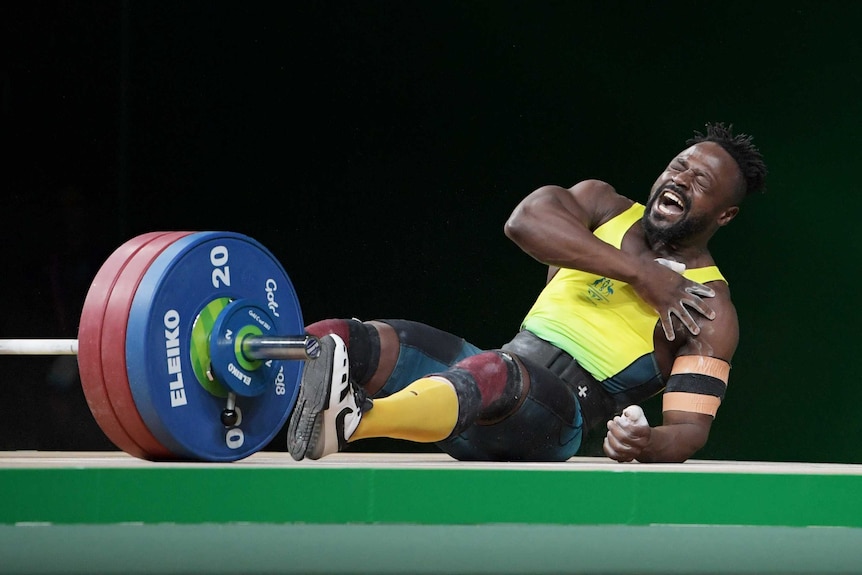 Weightlifter Francois Etoundi clutches his shoulder and falls to the ground