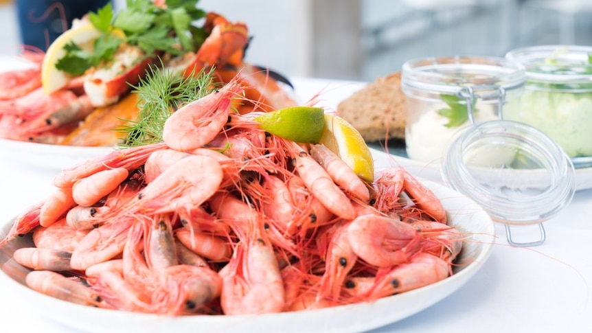 A big bowl of prawns on a kitchen bench with some sauces in jars and a plate of crab