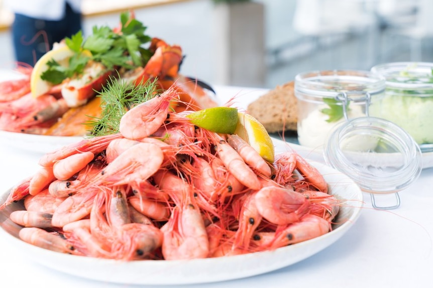 A big bowl of prawns on a kitchen bench with some sauces in jars and a plate of crab