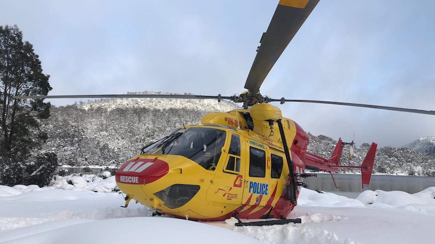 A red and yellow police chopper in the snow in front of a lake