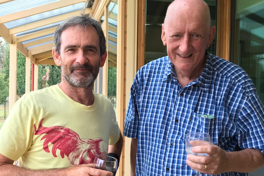 two men stand holding wine glasses