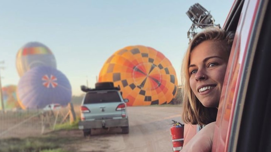 Balloon pilot Georgia Croft looking out of a car window with hot air balloons on the ground behind her