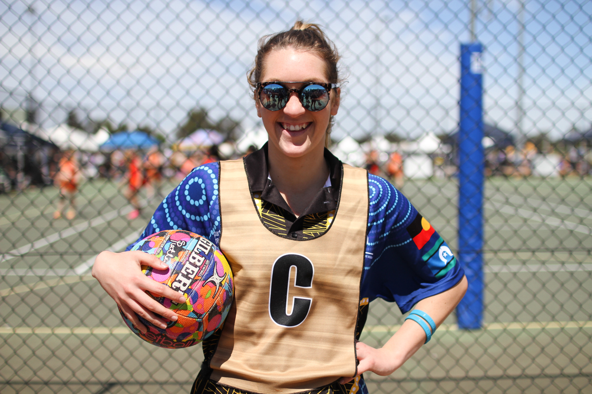 Nikki Bell 22, Team Beyond Blue Netball Team from Ballarat stands courtside holding  a netball under her arm.
