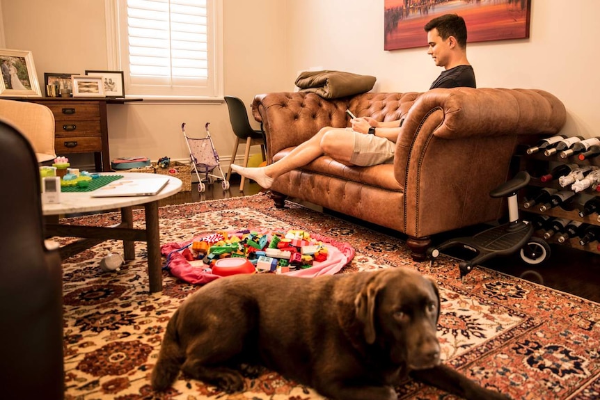 man on couch with toys and a brown dog on the ground
